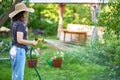 Young woman in hat watering flowers and plants in garden with hose in sunny blooming backyard Royalty Free Stock Photo