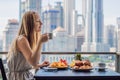 A young woman is having breakfast on the balcony. Breakfast table with coffee fruit and bread croisant on a balcony against the b