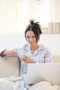 Young woman having breakfast in pyjama with laptop