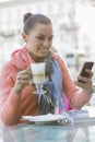 Young woman having coffee while using cell phone at sidewalk cafe Royalty Free Stock Photo