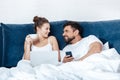 Young woman having coffee and using laptop with boyfriend in bed Royalty Free Stock Photo