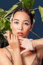 Freestyle. Young woman eyes decorated with perls wearing bracelet standing isolated on dark blue with plants posing