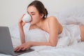 Young woman having good time in bed on the living room with coffee and laptop. Royalty Free Stock Photo