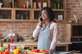 Young woman having pleasant conversation on phone while cooking