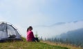 Young woman having a rest near tourist tent in the summer morning in the mountains Royalty Free Stock Photo