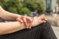 Young woman having rheumatoid arthritis takes a rest sitting on a bench at a park. Hands and legs are deformed. She feels pain.