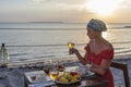 Young woman having romantic dinner in hotel restaurant during sunset near sea waves on the tropical beach, close up Royalty Free Stock Photo