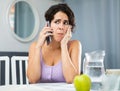 Young woman having toothache, sitting and using smartphone