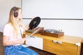 Young woman with headphones listens to music from vinyl records on a turntable at home.