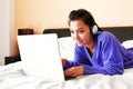 Young woman in headphones using a laptop in bed