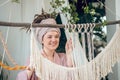 Young woman in a headwear looking contented while weaving macrame