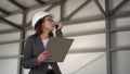 A young woman in a helmet with documents speaks on a walkie-talkie at a construction site. The boss woman in a suit