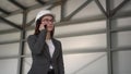 A young woman in a helmet speaks on the phone at a construction site. The boss in a suit is talking on the phone.