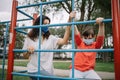 Young woman helping girl climb fence at playground with protection masks on faces