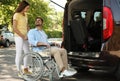 Young woman helping man in wheelchair to getinto van outdoors Royalty Free Stock Photo