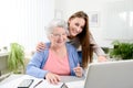 Young woman helping an old senior woman doing paperwork and administrative procedures with laptop computer at home