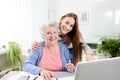 Young woman helping an old senior woman doing paperwork and administrative procedures with laptop computer at home Royalty Free Stock Photo