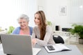 Young woman helping an old senior woman doing paperwork and administrative procedures with laptop computer at home Royalty Free Stock Photo