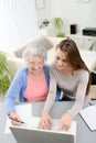 Young woman helping an old senior woman doing paperwork and administrative procedures with laptop computer at home Royalty Free Stock Photo