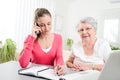 Young woman helping an old senior woman doing paperwork and administrative procedures with laptop computer at home