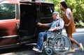 Young woman helping senior man in wheelchair to get into van Royalty Free Stock Photo