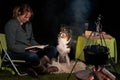 Young woman and her Australian Shepherd outside by a campfire. Reading a book at dusk. Bread, cheese and wine on the Royalty Free Stock Photo