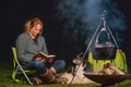 Young woman and her Australian Shepherd outside by a campfire. Reading a book at dusk. Bread, cheese and wine on the Royalty Free Stock Photo