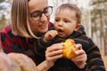 Young woman and her baby son in autumn park, boy playing with helloween pumpkin and eating pumpkin bun. Royalty Free Stock Photo