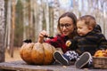 Young woman and her baby son in autumn park, boy playing with helloween pumpkin and eating pumpkin bun. Royalty Free Stock Photo