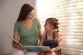 Young woman and her daughter reading book near window at home Royalty Free Stock Photo