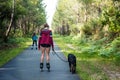 young woman rollerblading with her dog on a cycle path crossing the forest