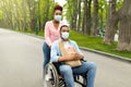 Young woman and her disabled boyfriend in wheelchair wearing face masks, walking through park during covid Royalty Free Stock Photo