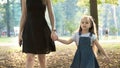 Young woman and her little daughter with long hair walking together holding hands in summer park Royalty Free Stock Photo