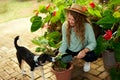 Young woman and her pet dog sitting in garden planting flowers in pots smiles and looks at camera. Female gardener with Royalty Free Stock Photo