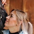 Girl blonde in blue quilted vest with ponytail plays with her horse, portraits of the woman with focus on her head close-up. Royalty Free Stock Photo