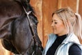 Girl blonde in blue quilted vest with ponytail plays with her horse, portraits of the woman with focus on her head close-up. Royalty Free Stock Photo