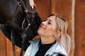 Girl blonde in blue quilted vest with ponytail plays with her horse, portraits of the woman with focus on her head close-up. Royalty Free Stock Photo