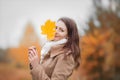 Young woman hides half face with autumn yellow maple leave.