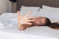 Young woman hides her face from the camera shy and smiling  lying on a bed in the bedroom and covered sheet. Royalty Free Stock Photo