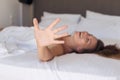 Young woman hides her face from the camera shy and smiling  lying on a bed in the bedroom and covered sheet. Royalty Free Stock Photo