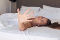 Young woman hides her face from the camera shy and smiling  lying on a bed in the bedroom and covered sheet. Royalty Free Stock Photo