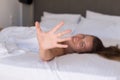 Young woman hides her face from the camera shy and smiling  lying on a bed in the bedroom and covered sheet. Royalty Free Stock Photo