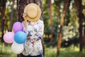 Young woman hiding behind straw hat with colorful air balloons on nature