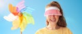 Young woman hiding behind sun visor holding colorful windmill Royalty Free Stock Photo