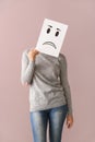 Young woman hiding face behind sheet of paper with drawn emoticon on color background Royalty Free Stock Photo