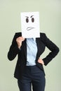 Young woman hiding face behind sheet of paper with drawn emoticon on light background Royalty Free Stock Photo