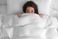 Young woman hiding under warm white blanket in bed, top view Royalty Free Stock Photo