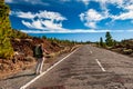 Young woman hiker with backpack from behind standing on wayside of road and hitchhiking near Pico del Teide mountain in El Teide Royalty Free Stock Photo