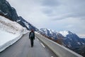 Young woman hiker with backpack walking up on a mountain road with large snowdrifts, springtime, back view. Royalty Free Stock Photo