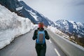 Young woman hiker with backpack walking up on a mountain road with large snowdrifts, springtime, back view. Royalty Free Stock Photo